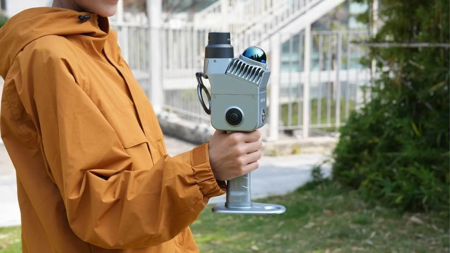 XGRIDS のハンディ型3Dスキャナ Lixel K2。上部に回転式の LiDAR と広角カメラが載った本体を、屋外で片手に持って歩きながら計測している